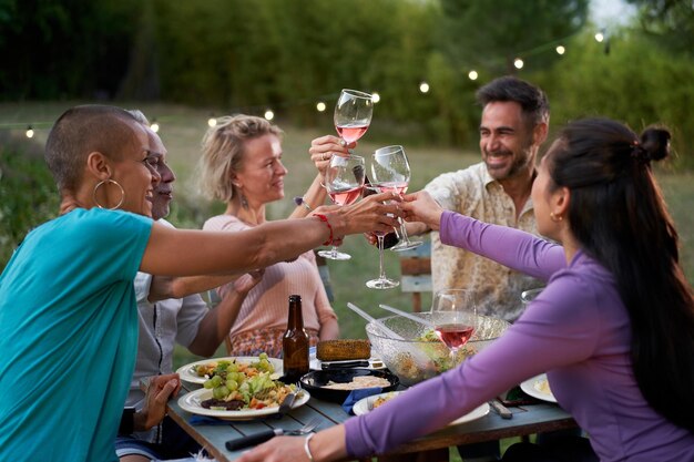 Amigos felices divirtiéndose bebiendo vino rojo en el patio trasero en una cena privada.