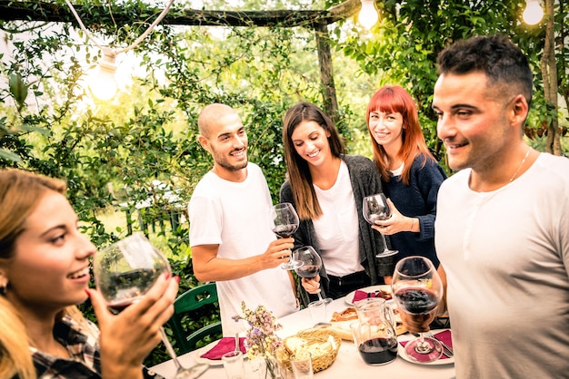 Amigos felices divirtiéndose bebiendo vino tinto en la fiesta en el jardín del patio trasero