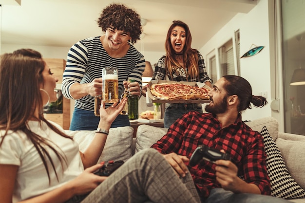 Amigos felices divirtiéndose mientras comen pizza y beben cerveza. Tienen un gran fin de semana en buena compañía en el interior.