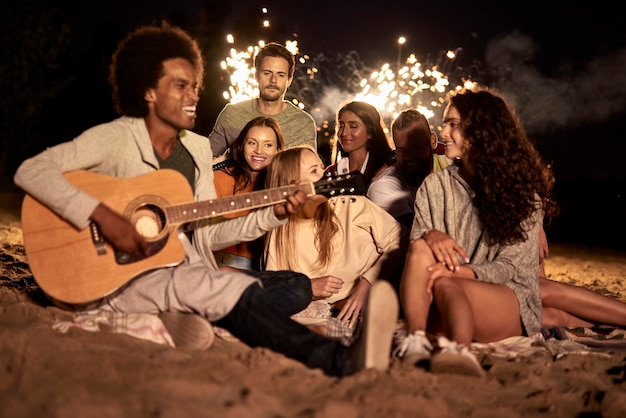 Amigos felices divirtiéndose en la playa por la noche