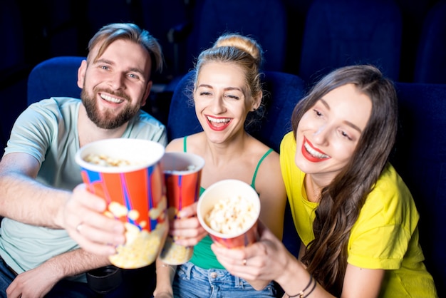 Amigos felices divirtiéndose sentados junto con palomitas de maíz en el cine