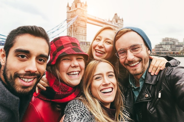 Amigos felices divirtiéndose tomándose selfie con teléfono móvil en Londres con el Tower Bridge en el fondo Centrándose en la cara de la chica del centro