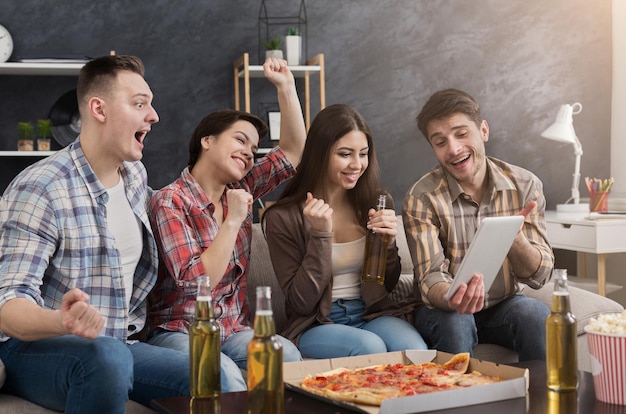 Amigos felices de fiesta y viendo videos divertidos en tableta en casa