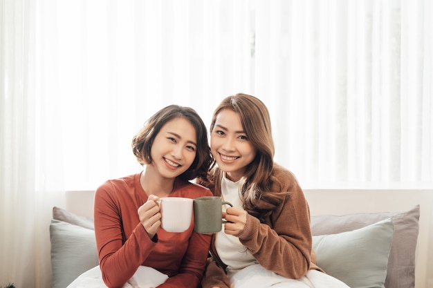 Amigos felices hablando y bebiendo café y té sentados en un sofá en casa