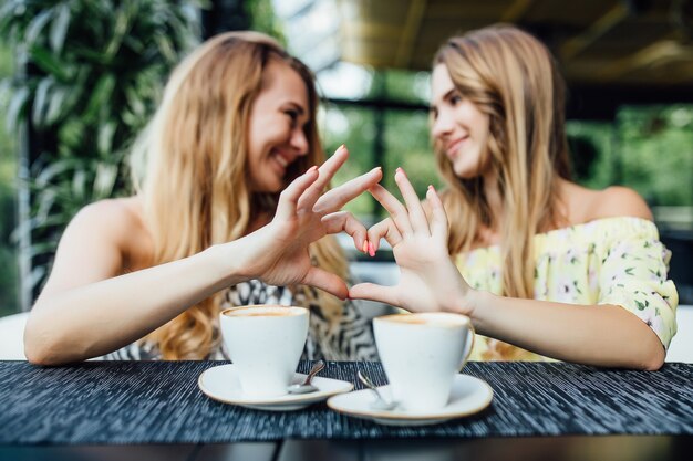 Amigos felices haciendo gesto de corazón y tomando café en la terraza