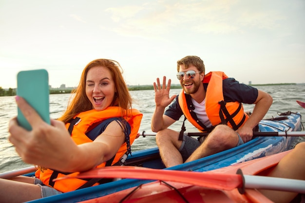 Amigos felices en kayak en el río con puesta de sol en el fondo