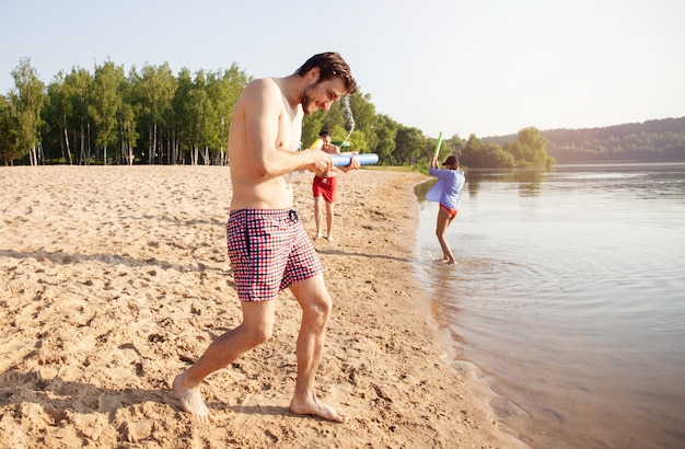 Amigos felices luchando con pistolas de agua - Juventud, estilo de vida de verano y concepto de vacaciones