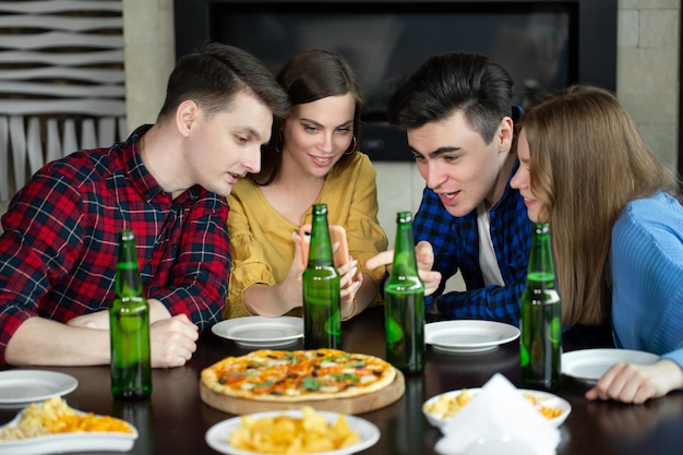 Amigos felices miran el teléfono mientras beben cerveza y pizza en un café