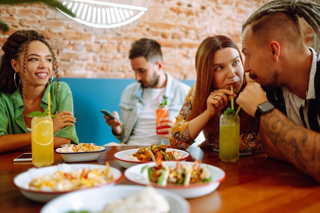 Foto amigos felices pasando un buen rato en el café jóvenes sentados en un restaurante divirtiéndose juntos