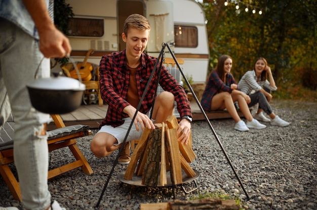 Amigos felices se prepara para cocinar en una fogata, hacer un picnic en el campamento en el bosque. Los jóvenes tienen una aventura de verano en autocaravana, autocaravana Ocios para dos parejas, viajando con remolque