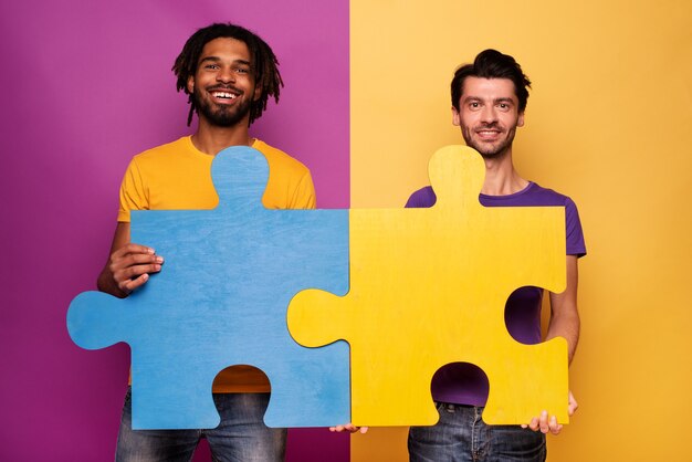 Amigos felices con rompecabezas en la mano sobre amarillo. Concepto de integración, unión y asociación