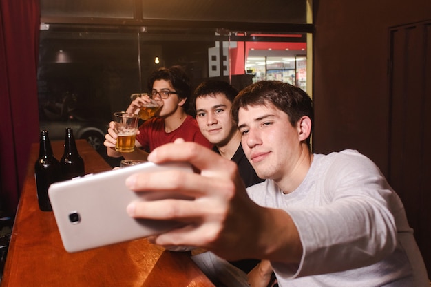 Amigos felices tomando un selfie mientras beben cerveza en el bar.