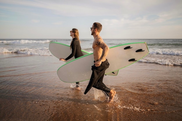 Amigos felizes a surfar juntos na praia a correr com pranchas de surf perto do oceano