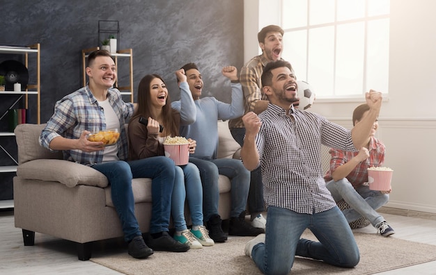 Amigos felizes assistindo jogo de futebol e comendo pipoca em casa