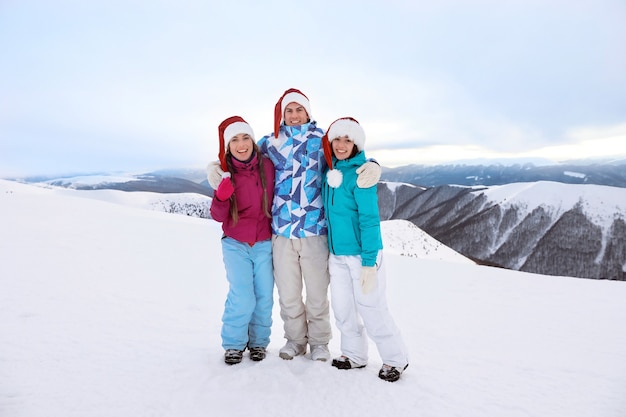 Amigos felizes com chapéus de papai noel no pico nevado de uma montanha no resort