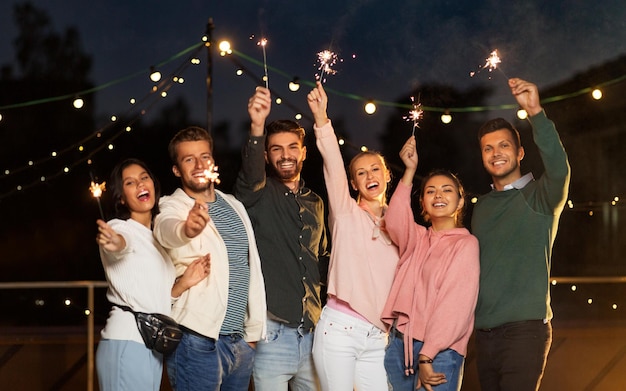 Amigos felizes com faíscas numa festa no telhado.