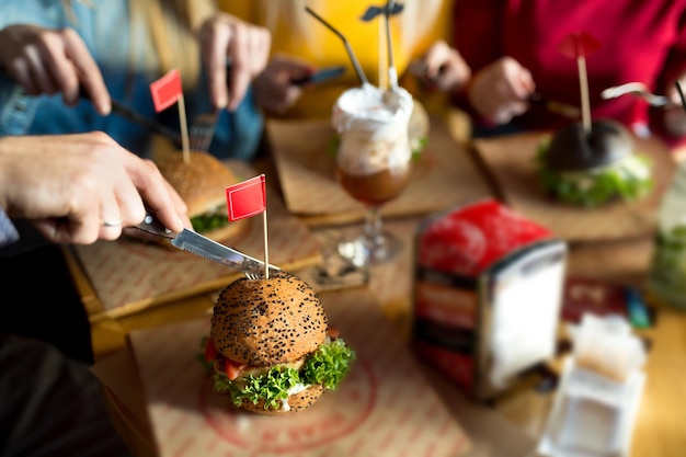 Amigos felizes cortam um hambúrguer com uma faca em um restaurante e riem.