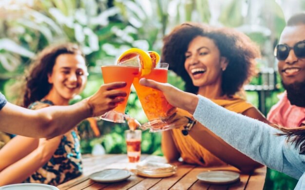 Amigos felizes de várias raças brindando com copos de coquetel ao ar livre nas férias de verão