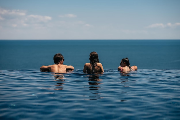 Amigos felizes nadando na piscina infinita à beira-mar