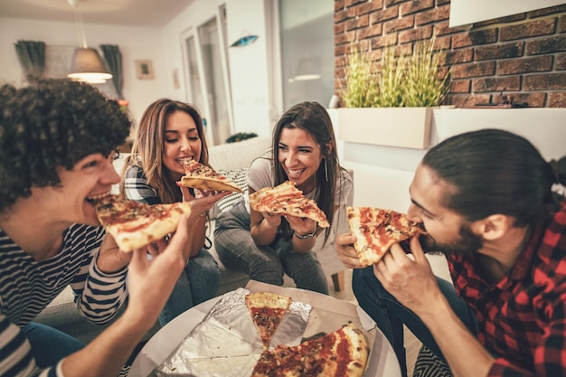 Foto amigos felizes se divertindo enquanto come pizza. eles têm um ótimo fim de semana em boa companhia dentro de casa.