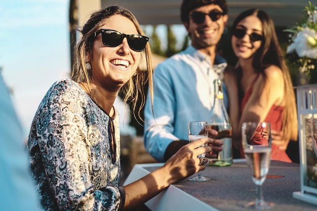 Amigos felizes se reunindo na festa do terraço se divertindo e bebendo vinho branco espumante conceito de estilo de vida de jovens frequentando o fim de semana conversando e consumindo bebidas alcoólicas