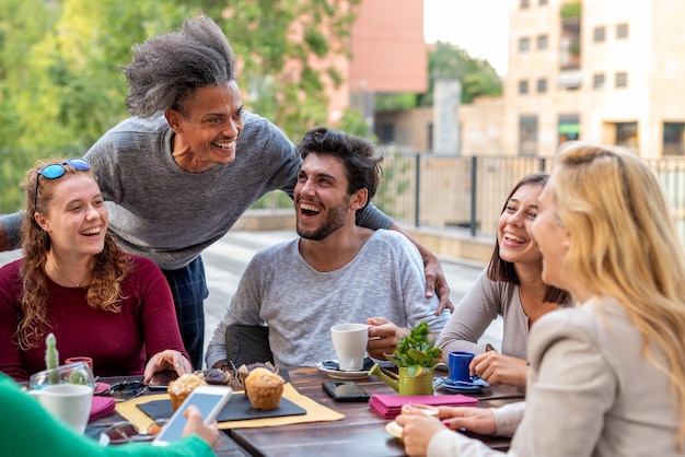 Amigos felizes tomando café da manhã entre pessoas de diferentes grupos étnicos na mesa de um bar de confeitaria estudantes no intervalo bebendo café e cappuccino e comendo muffins