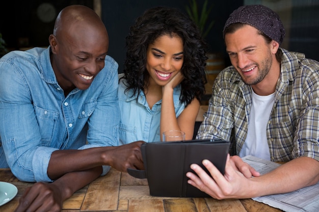 Amigos felizes usando tablet digital na mesa de uma cafeteria