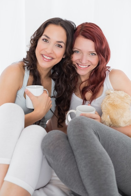 Amigos femeninos jovenes felices con las tazas de café en cama