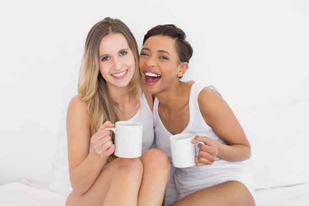 Amigos femininos alegres com copos de café na cama