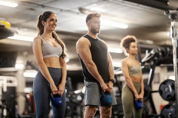 Amigos en forma de pie en un gimnasio y haciendo ejercicio con kettlebells