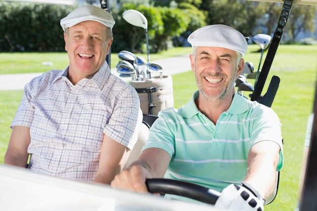 Amigos de golf conduciendo en su carrito de golf sonriendo a la cámara