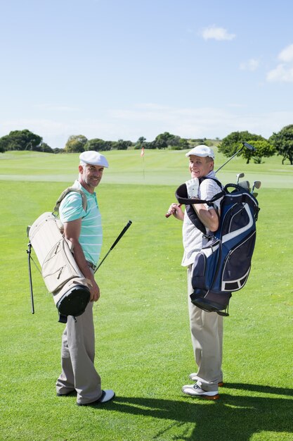 Amigos del golfista que sonríen en la cámara que sostiene sus bolsos del golf