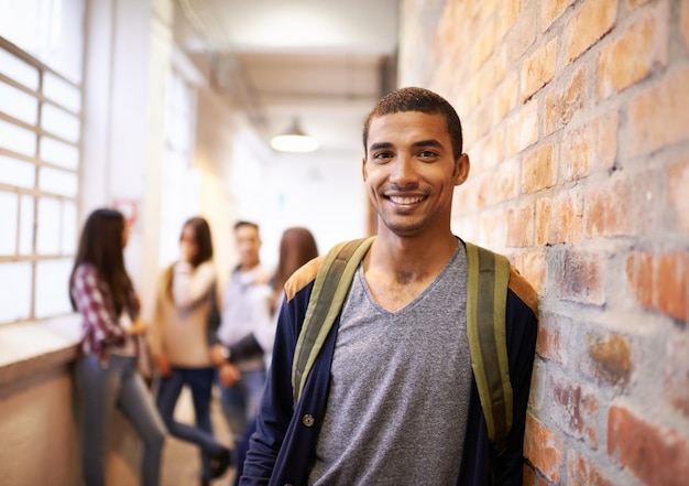 Los amigos hacen que la universidad sea divertida Retrato de un apuesto joven estudiante apoyado contra una pared con sus amigos en el fondo