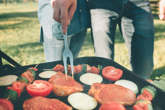 Amigos haciendo barbacoa y almorzando en la naturaleza. Pareja divirtiéndose mientras come y bebe en un picnic - Gente feliz en la fiesta de barbacoa.