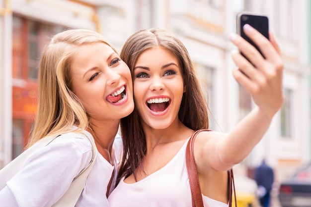 Amigos haciendo selfie. Dos hermosas mujeres jóvenes haciendo selfie y haciendo muecas