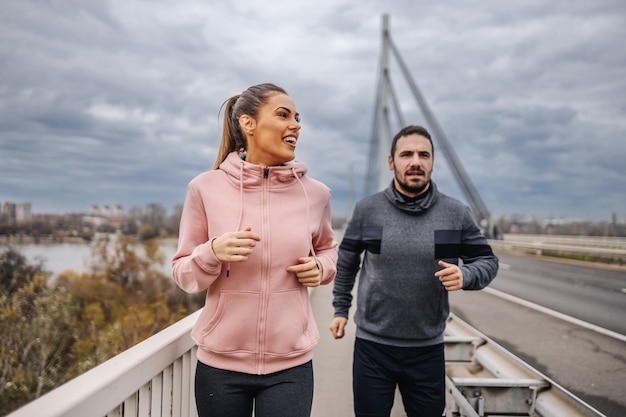 Amigos heterosexuales deportivos apuestos en ropa deportiva para correr en el puente. Exterior urbano. Concepto de fitness al aire libre.