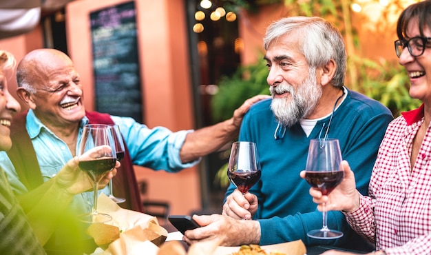 Amigos idosos felizes se divertindo bebendo vinho tinto no jantar