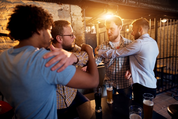 Foto amigos impedindo a briga de dois caras bravos no bar.