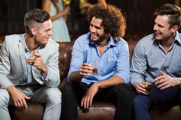 Amigos interagindo uns com os outros enquanto bebem charuto e uísque no bar