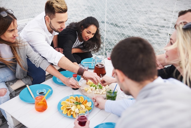 Amigos jóvenes felices estaban sentados en una mesa y haciendo un picnic al aire libre.