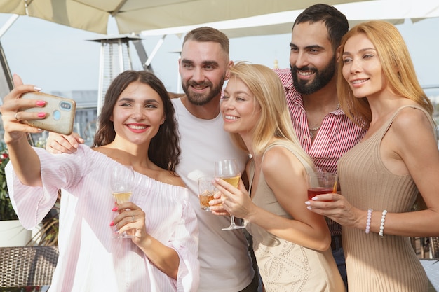 Foto amigos jóvenes felices tomando selfies durante la fiesta en la azotea