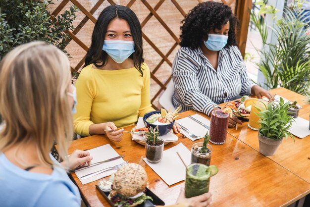 Amigos jóvenes multirraciales felices comiendo en el restaurante de brunch durante el brote de coronavirus - Concéntrese en la cara de la niña asiática