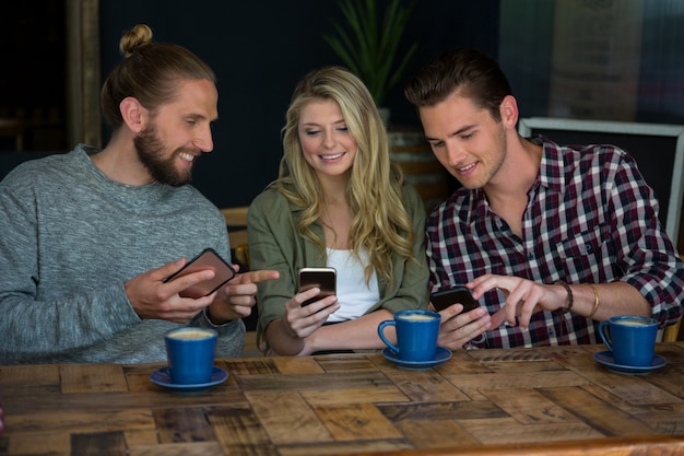 Amigos jóvenes sonrientes con teléfonos inteligentes en la mesa de café