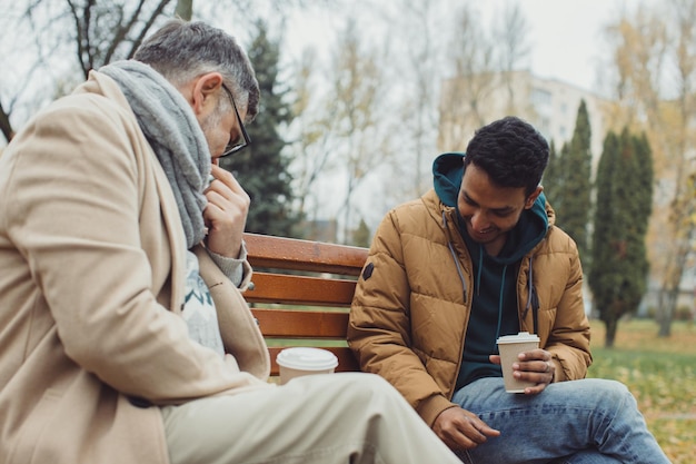 Amigos juegan al ajedrez en un banco en un parque de otoño Amistad multicultural de personas de diferentes edades