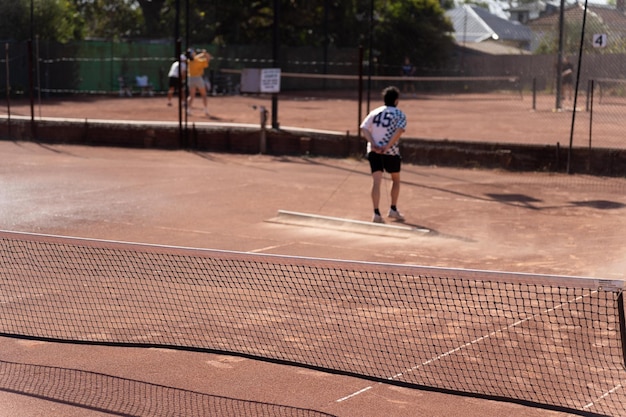 amigos jugando al tenis en una cancha de arcilla regando y embolsando una canca de arcilla haciendo mantenimiento de la cancha de tenis