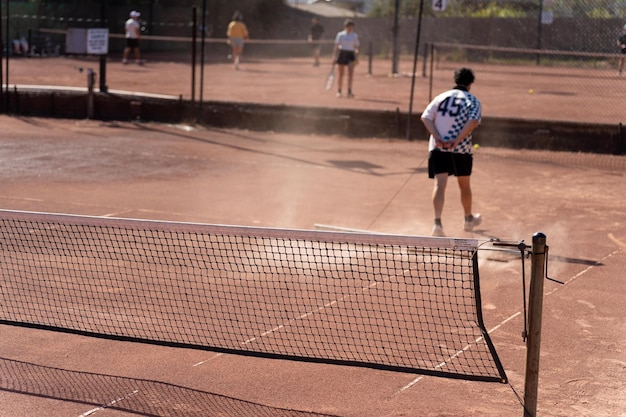 amigos jugando al tenis en una cancha de arcilla regando y embolsando una canca de arcilla haciendo mantenimiento de la cancha de tenis