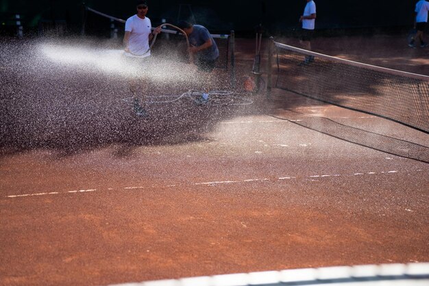 amigos jugando al tenis en una cancha de arcilla regando y embolsando una canca de arcilla haciendo mantenimiento de la cancha de tenis