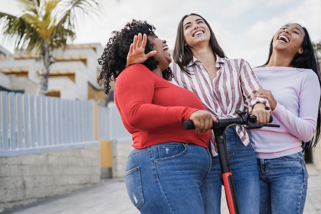 Amigos latinos felices divirtiéndose con scooter eléctrico al aire libre en la ciudad - Centrarse en la cara de niña del centro