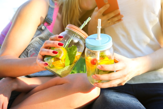 Amigos con limonada fresca en frascos con pajitas. Fiesta de verano hipster con bebidas. Estilo de vida vegano saludable. Ecológico en la naturaleza. Limones, naranjas y bayas con menta en el vaso.