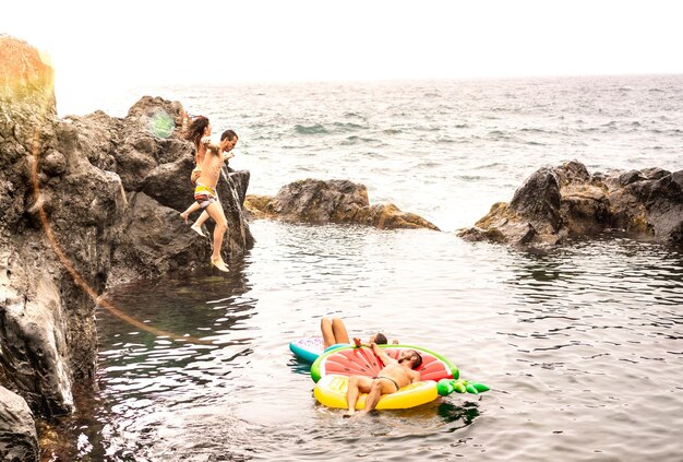 Amigos locos vacacionistas saltando en la piscina natural en la ubicación de la playa de viaje